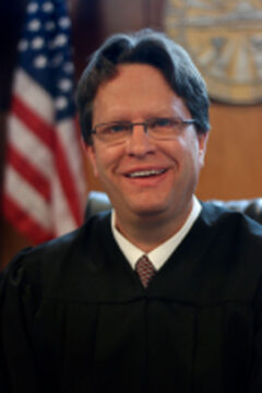 Smiling judge in robe with American flag.